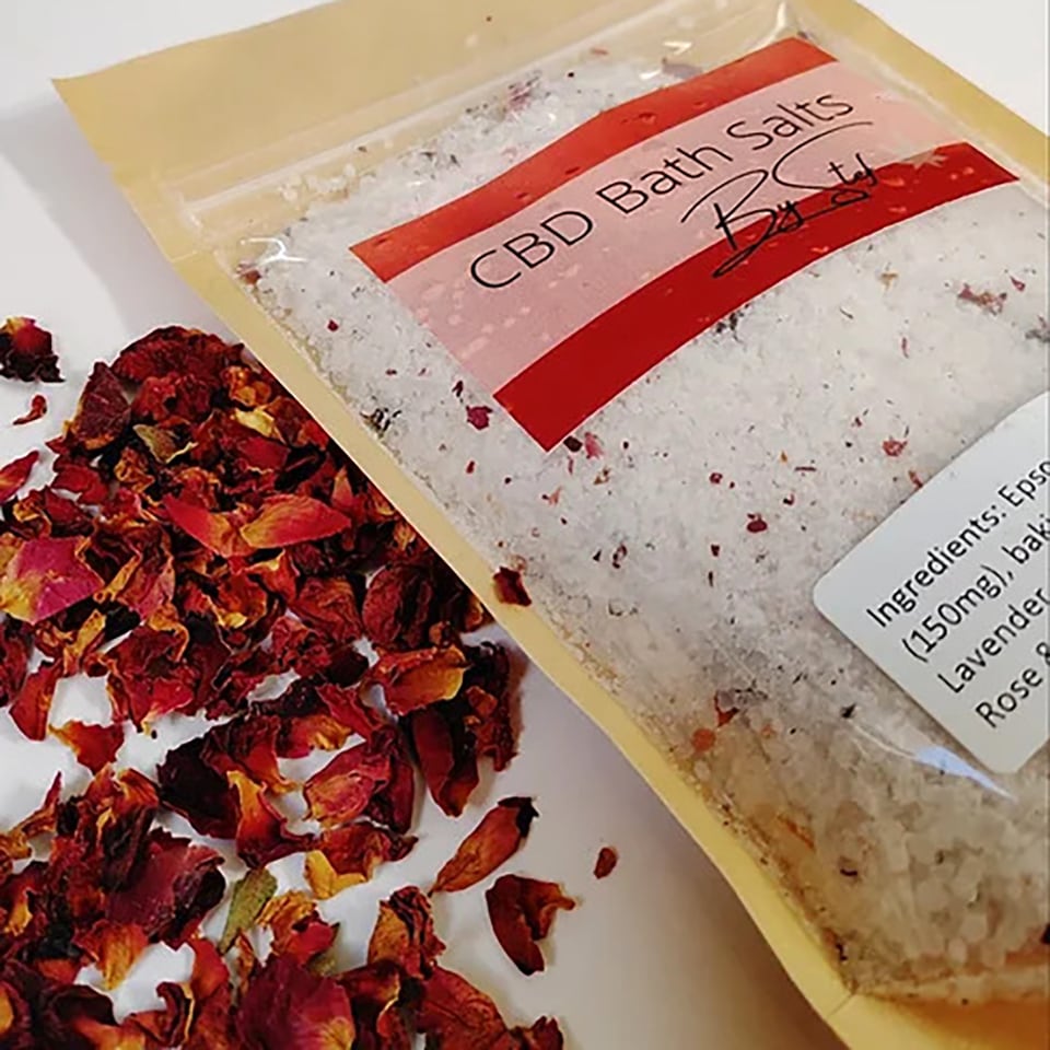 Bag of CBD-infused bath salts laying next to dried flower petals